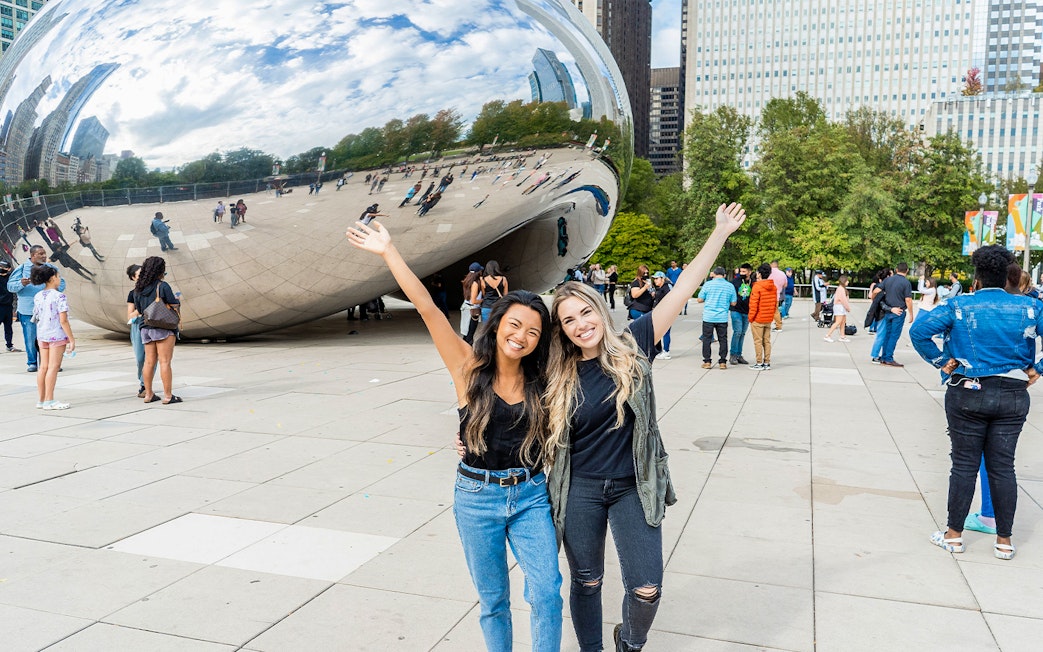 Tourists smiling in front of Cloud Gate sculpture in Chicago.