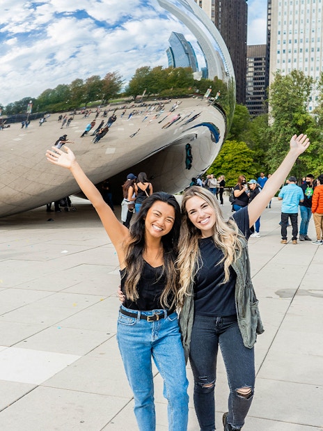 Tourists smiling in front of Cloud Gate sculpture in Chicago.