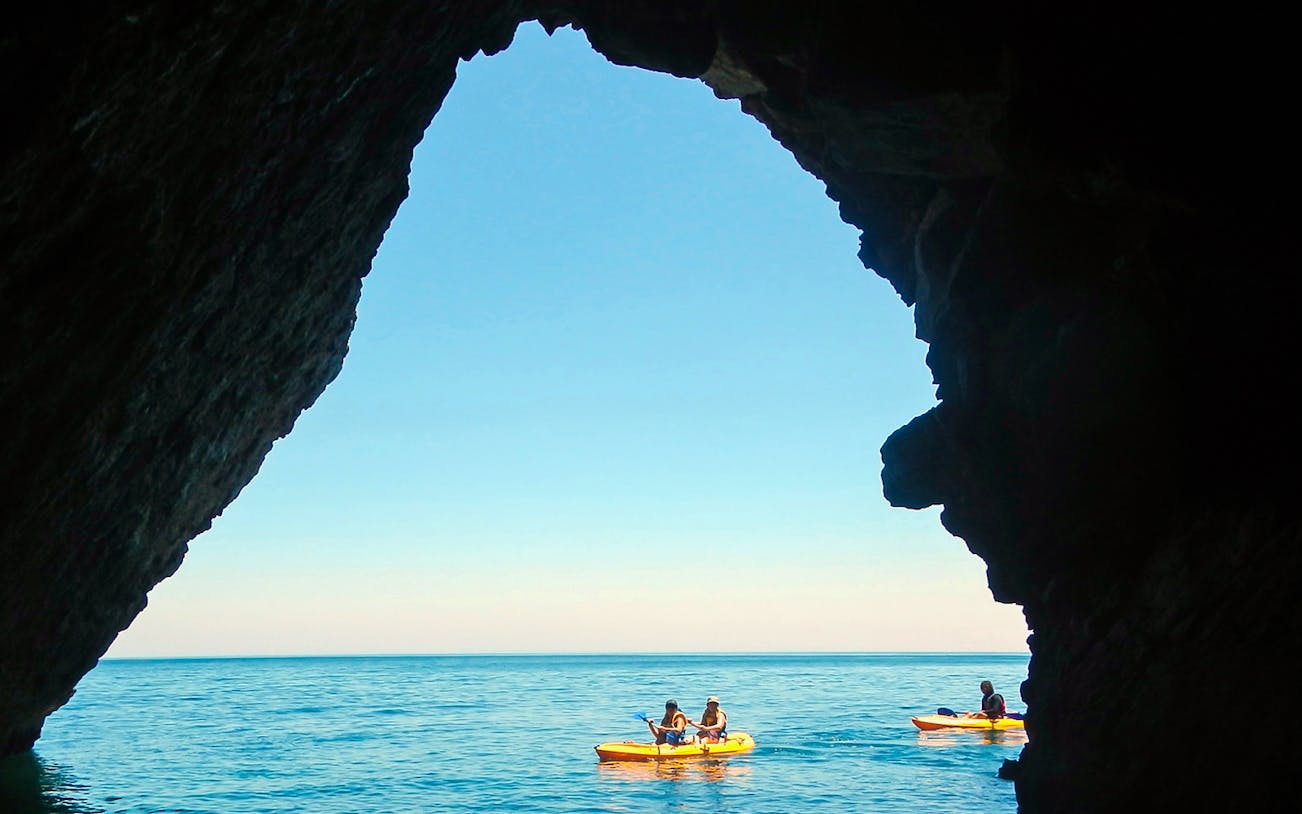Kayakers paddling in clear waters of Arrábida Natural Park, Lisbon, with rocky cliffs in the background.