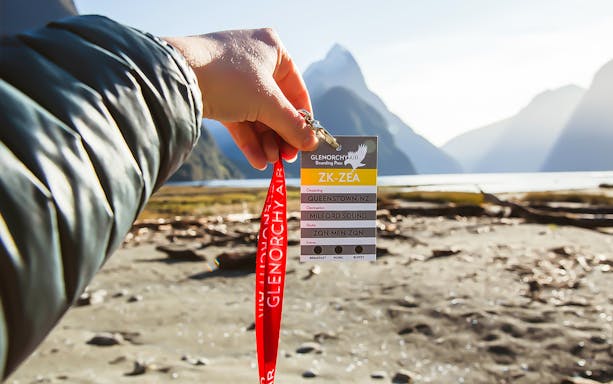 Boarding pass for scenic flight from Queenstown to Milford Sound, held with mountain view.