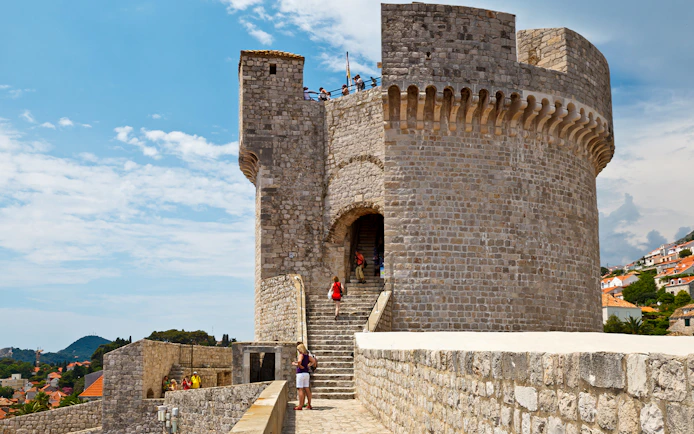 Stone fortress wall with tourists exploring, part of the Walls & Wars Tour in Dubrovnik, Croatia.