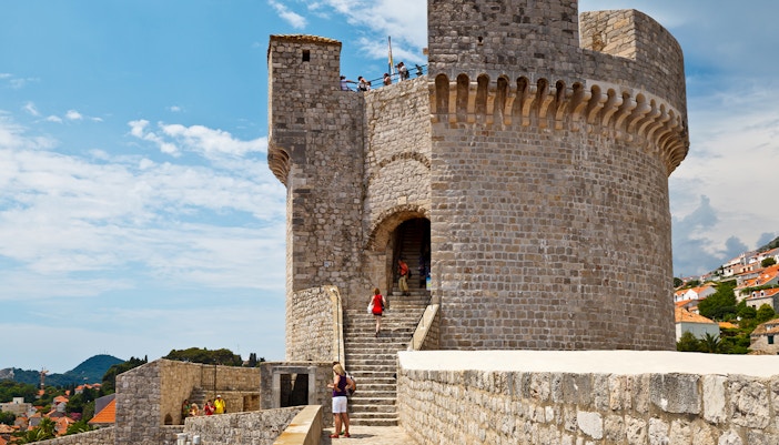 Stone fortress wall with tourists exploring, part of the Walls & Wars Tour in Dubrovnik, Croatia.