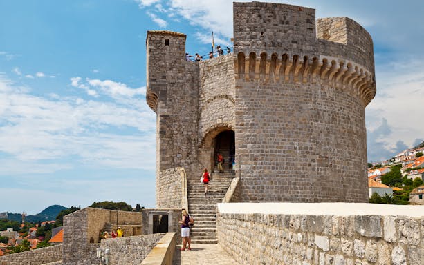 Stone fortress wall with tourists exploring, part of the Walls & Wars Tour in Dubrovnik, Croatia.