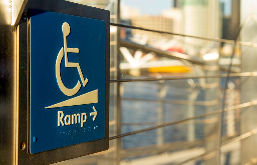 Wheelchair access ramp sign with cityscape background.