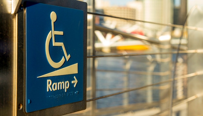 Wheelchair access ramp sign with cityscape background.