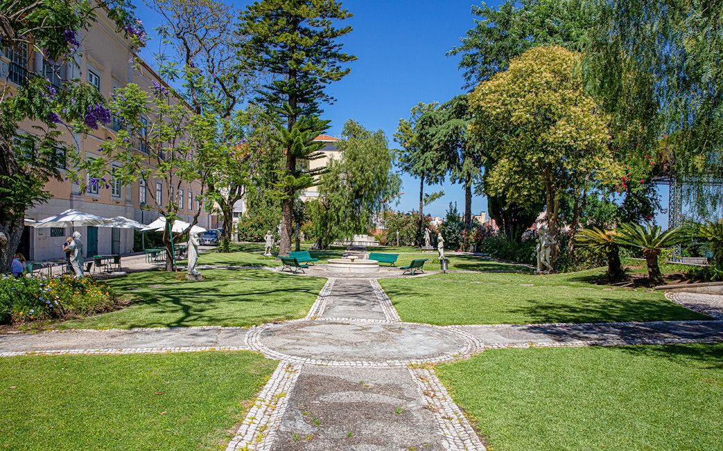 Garden view at the National Museum of Ancient Art, Lisbon, with statues and greenery.