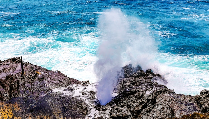 Halona Blow Hole in Oahu, Hawaii, with ocean waves crashing against rocky shore.
