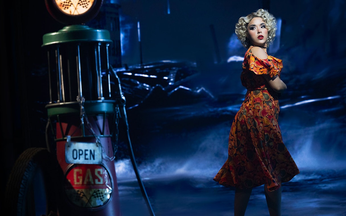 Woman in vintage dress near gas pump, The Great Gatsby theme.