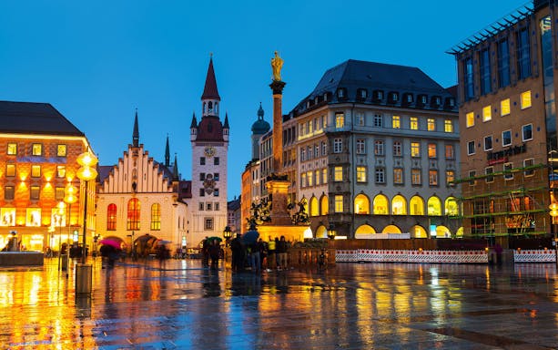 Marienplatz in Munich at dusk with illuminated buildings and people walking.