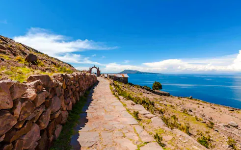 Stone path leading to archway on Taquile Island, Lake Titicaca, with distant mountains and blue sky.