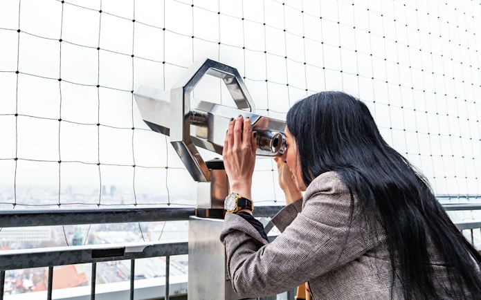 Woman using binoculars to view Berlin TV Tower from observation deck.