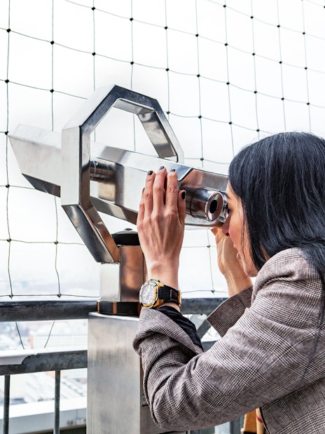 Woman using binoculars to view Berlin TV Tower from observation deck.