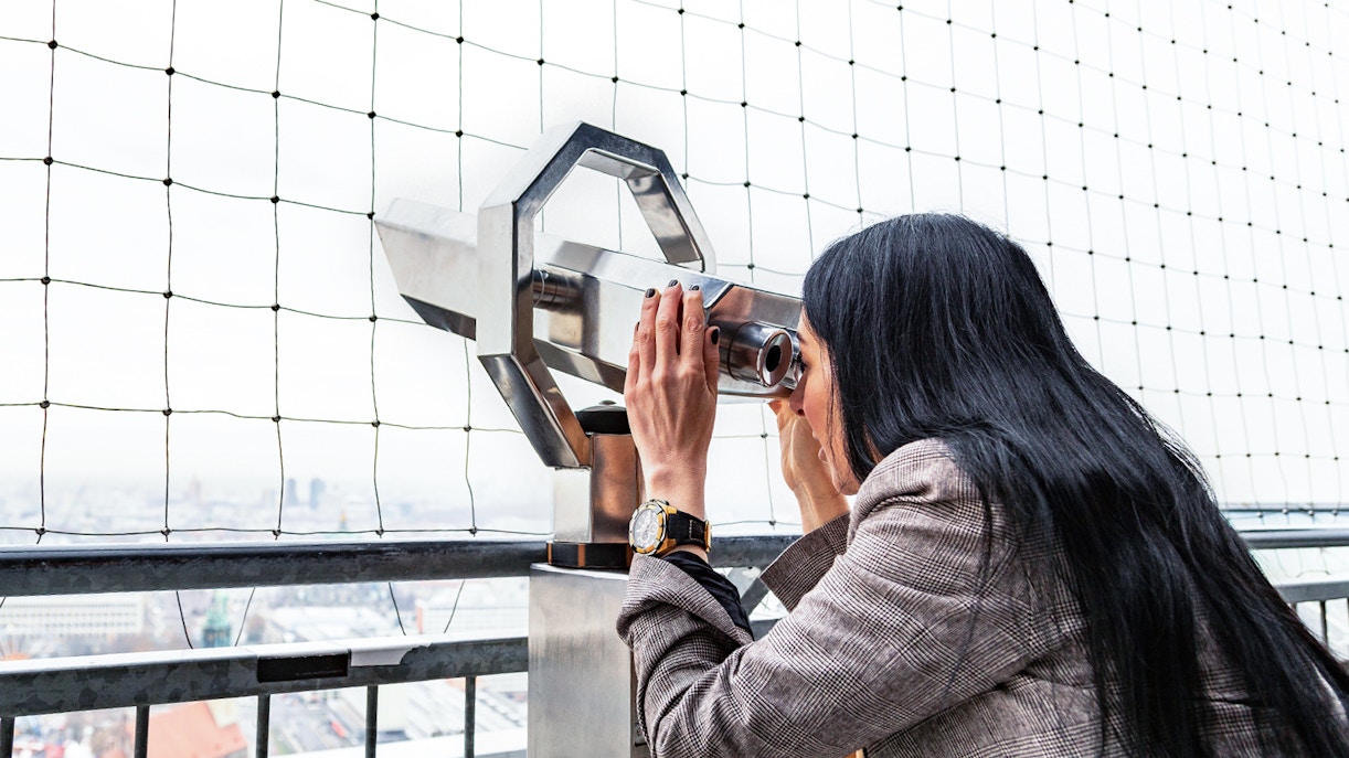 Eine Frau blickt durch ein Fernglas am Berliner Fernsehturm
