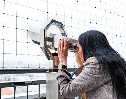 Woman using binoculars to view Berlin TV Tower from observation deck.