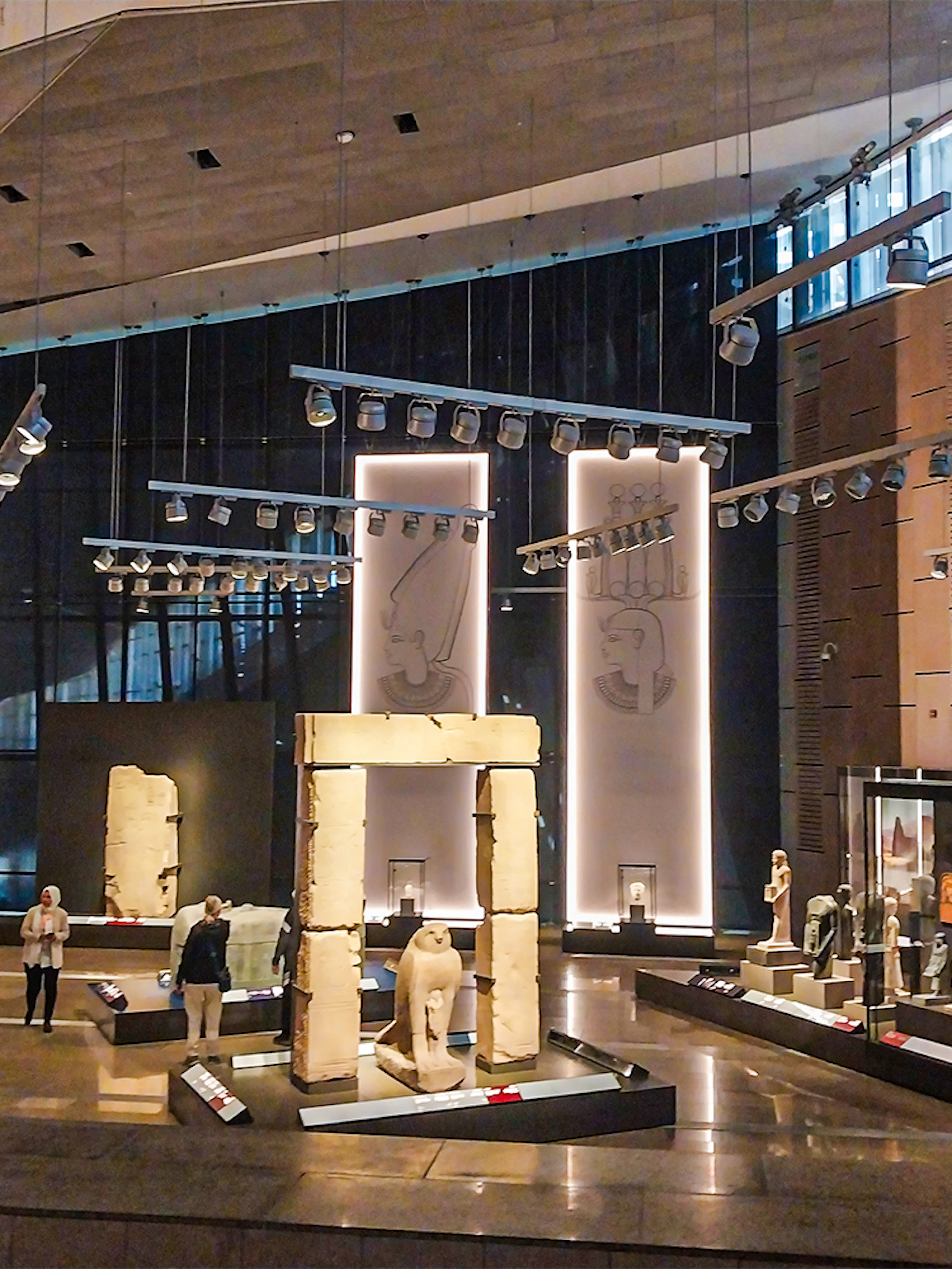 A wide angle shot of the interior of the Grand Egyptian Museum, where people are viewing statues and artefacts in the glass sheletered museum