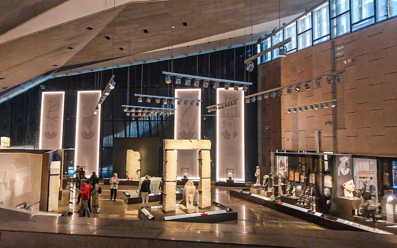 A wide angle shot of the interior of the Grand Egyptian Museum, where people are viewing statues and artefacts in the glass sheletered museum