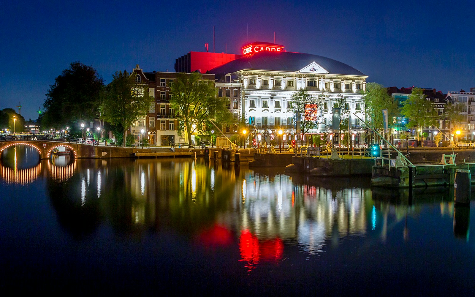 Royal Theater Carré illuminated at night, reflecting in Amsterdam canal.