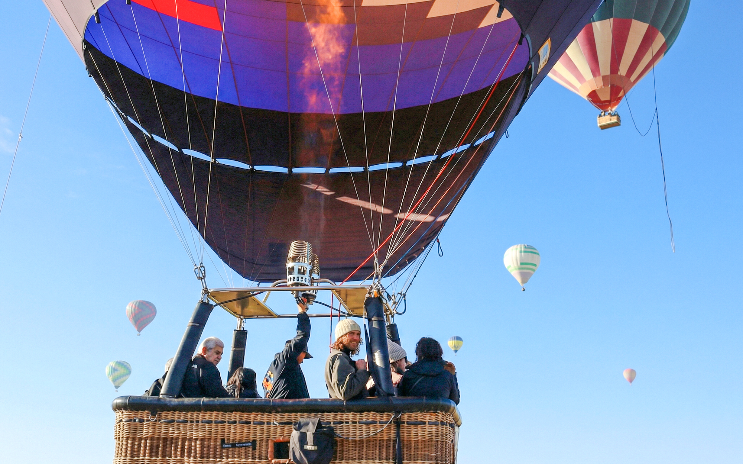 Hot air balloon with passengers ascending over Mexico City, multiple balloons in the sky.