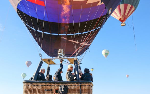 Hot air balloon with passengers ascending over Mexico City, multiple balloons in the sky.