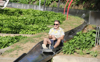 Man riding toboggan at Mutianyu Great Wall, surrounded by greenery.
