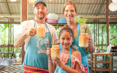 Family enjoying Thai iced tea at Mama Noi Cooking Class in organic garden.