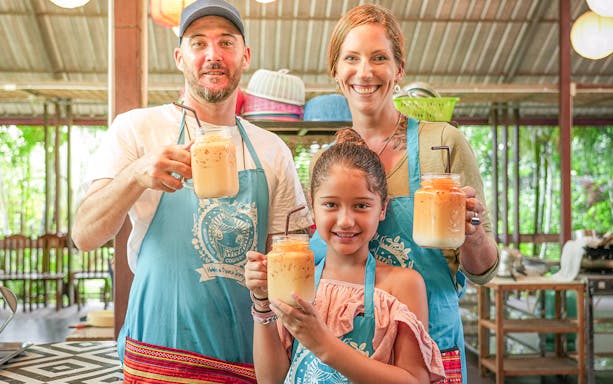 Family enjoying Thai iced tea at Mama Noi Cooking Class in organic garden.