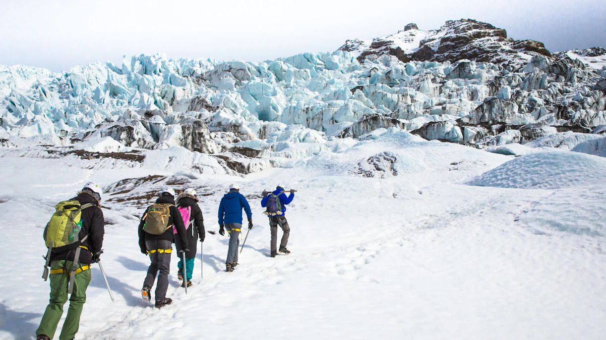 Group hiking on Iceland glacier with ice formations in the background.