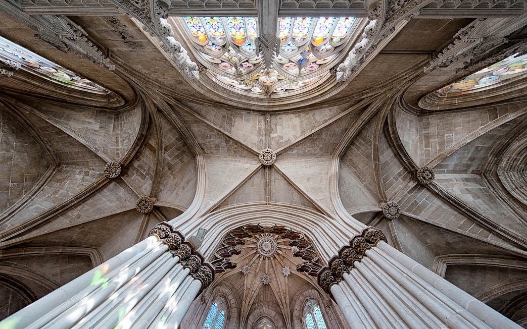 Batalha Monastery ceiling with intricate stone arches and stained glass windows.
