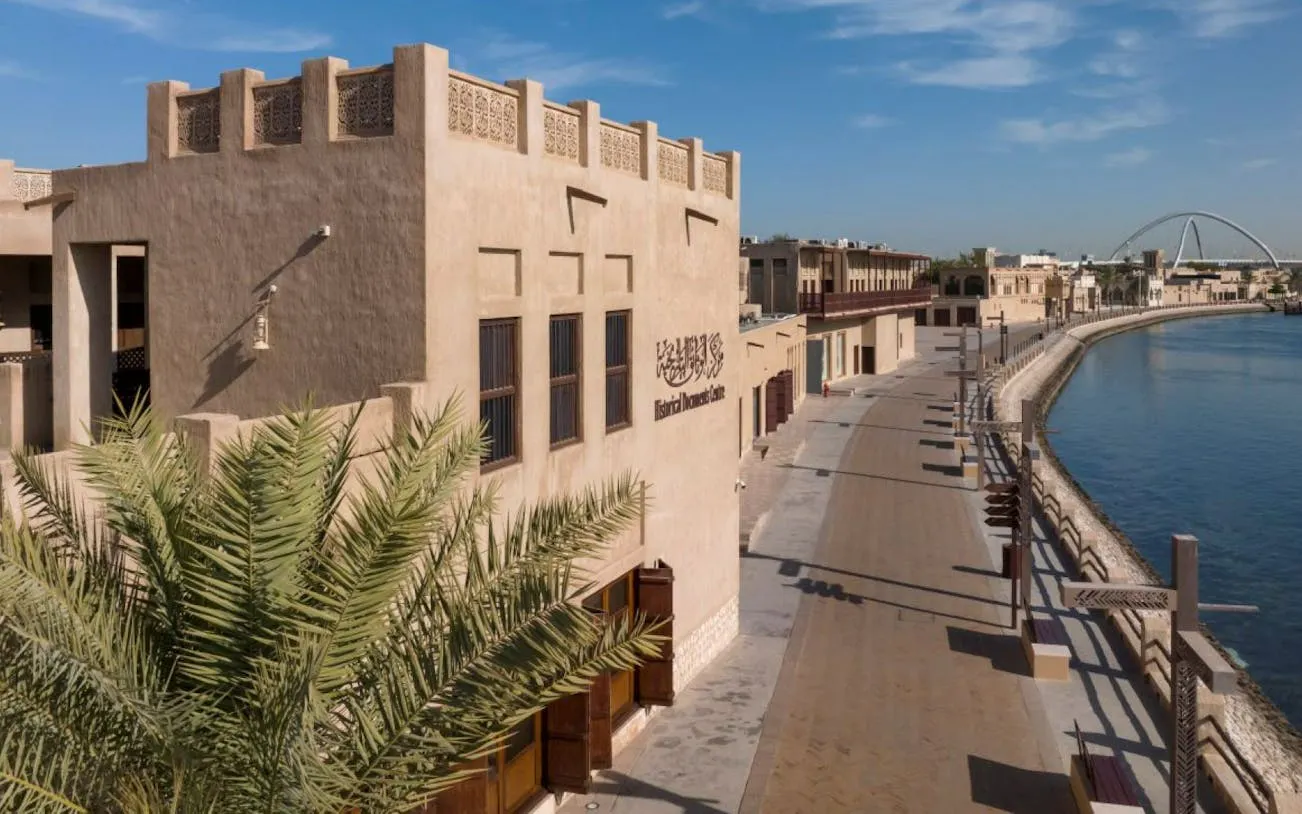 Heritage site along Dubai Creek with traditional architecture and palm trees.