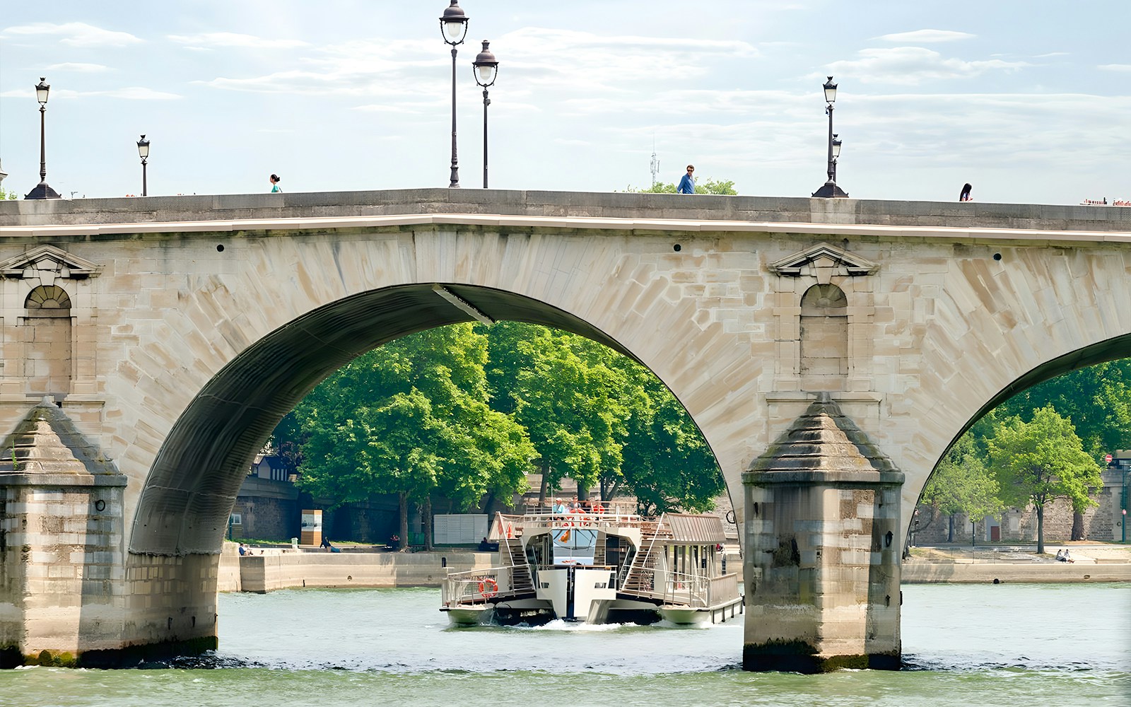 Seine River cruise boat passing under a stone bridge in Paris.