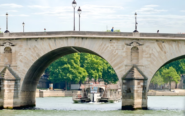 Seine River cruise boat passing under a stone bridge in Paris.
