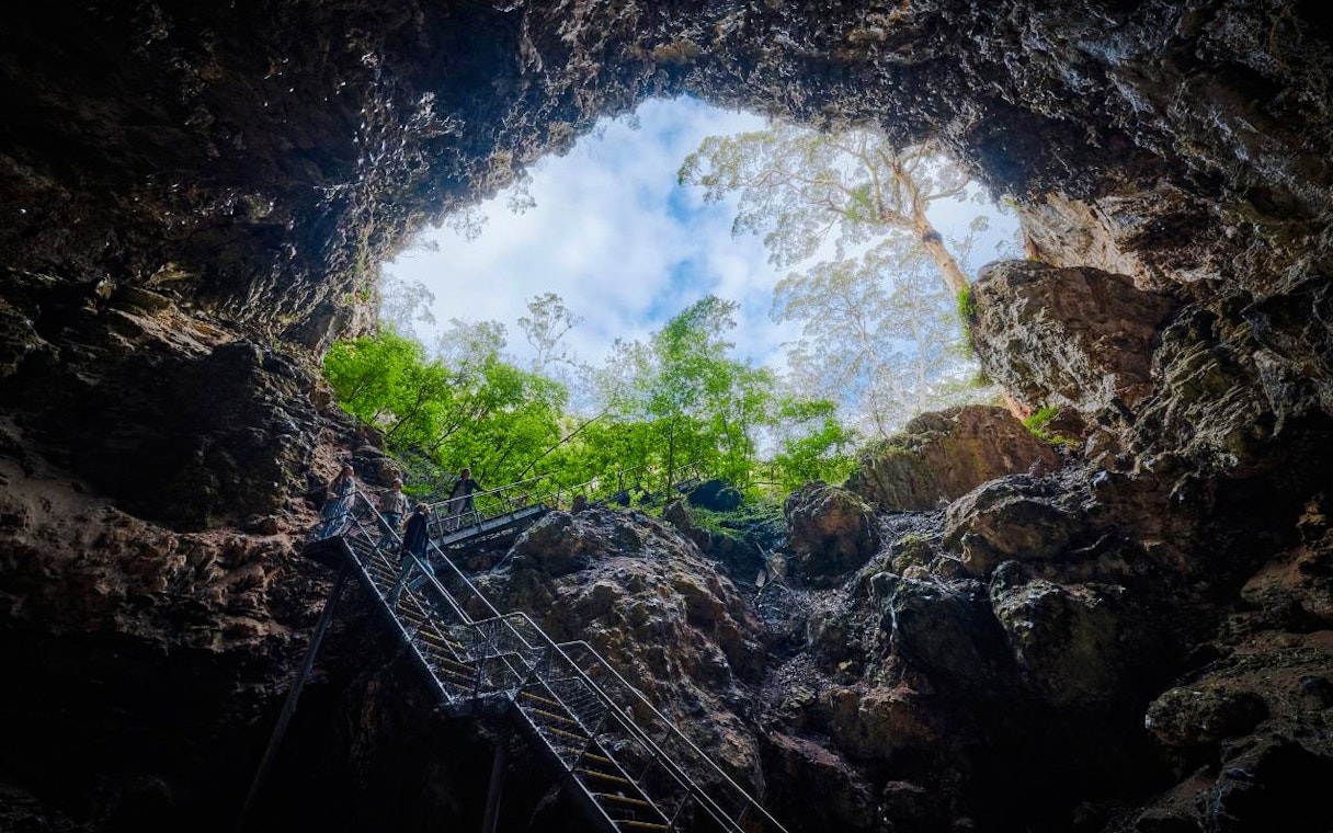 Visitors exploring Margaret River Cave via metal staircase, surrounded by rock formations and greenery.