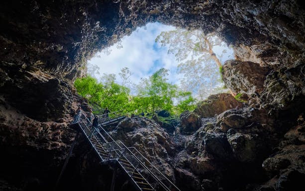 Visitors exploring Margaret River Cave via metal staircase, surrounded by rock formations and greenery.