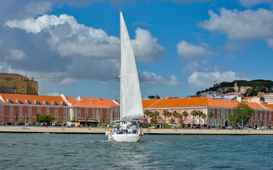 Sailboat on Tagus River with Lisbon's colorful buildings in the background.