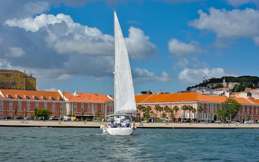 Sailboat on Tagus River with Lisbon's colorful buildings in the background.