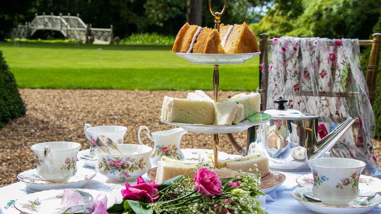 Afternoon tea setup with tiered sandwich platter and floral teacups in a garden setting.