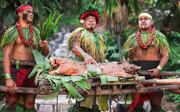 Traditional pig roast at Chief's Luau, Oahu, Hawaii with performers in cultural attire.