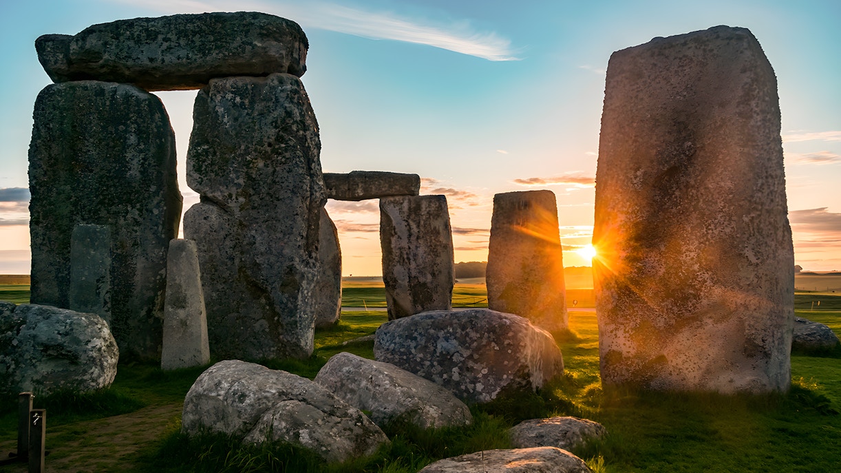 Stonehenge at sunset with sun rays peeking through ancient stone formations.