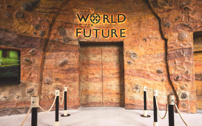 Entrance to exhibit with "Better World Better Future" sign on textured stone wall.