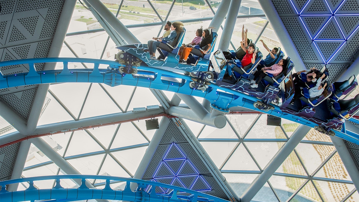 Riders on The Storm Coaster in Dubai inside a futuristic glass structure.