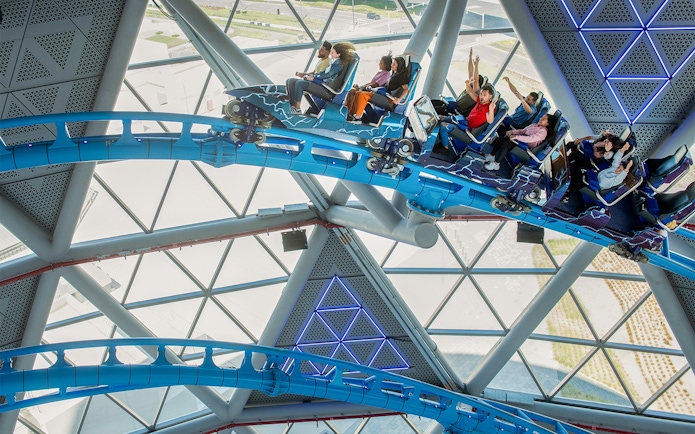 Riders on The Storm Coaster in Dubai inside a futuristic glass structure.