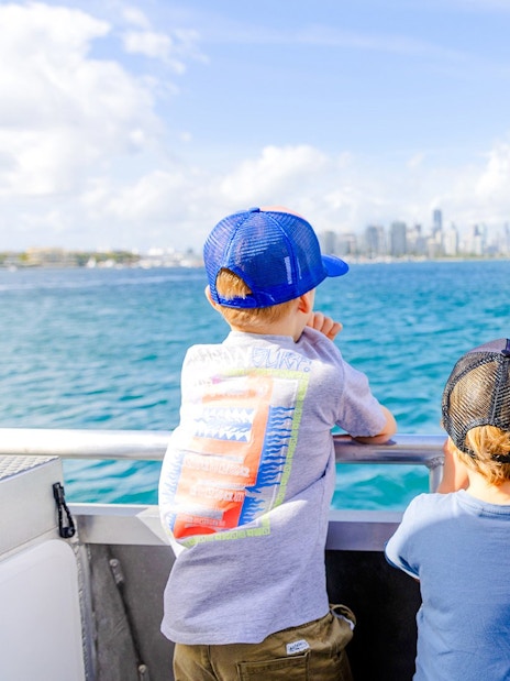 Kids and parents enjoying Gold Coast Hop-on Hop-off Boat Tour with city skyline in view.