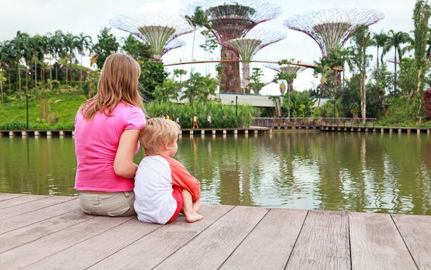 Visitors sitting by the water at Gardens by the Bay with Supertree Grove in view.