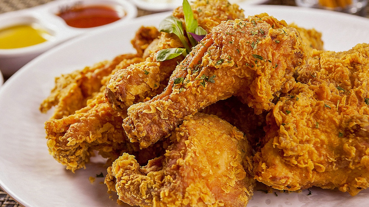 Korean fried chicken drumsticks on a white plate with dipping sauces in the background.