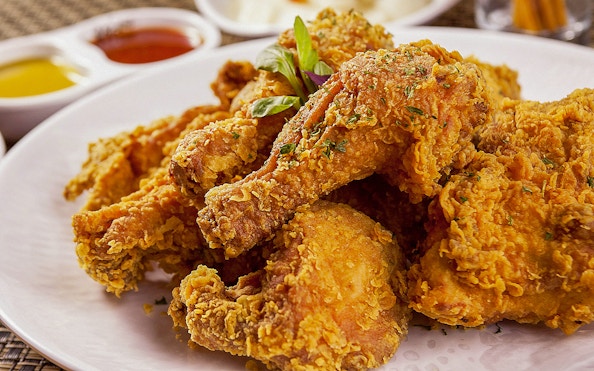 Korean fried chicken drumsticks on a white plate with dipping sauces in the background.