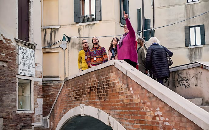 Tour group on a bridge in Venice's Castello district, guide pointing out landmarks.