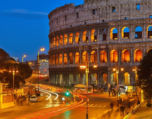 Colosseum illuminated at night with street lights and traffic in Rome, Italy.