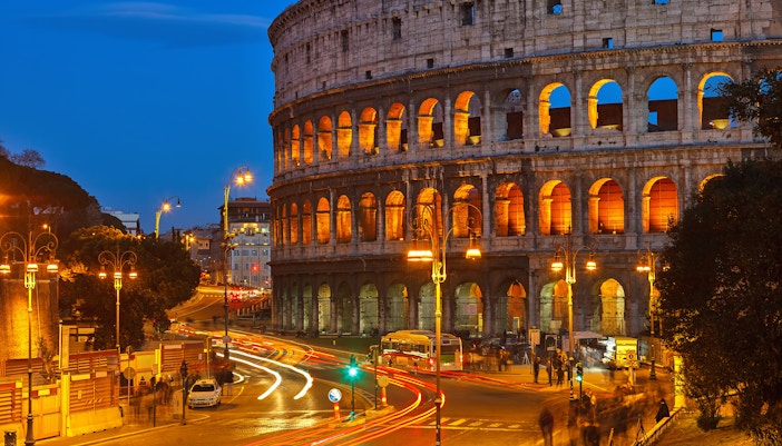 Colosseum illuminated at night with street lights and traffic in Rome, Italy.