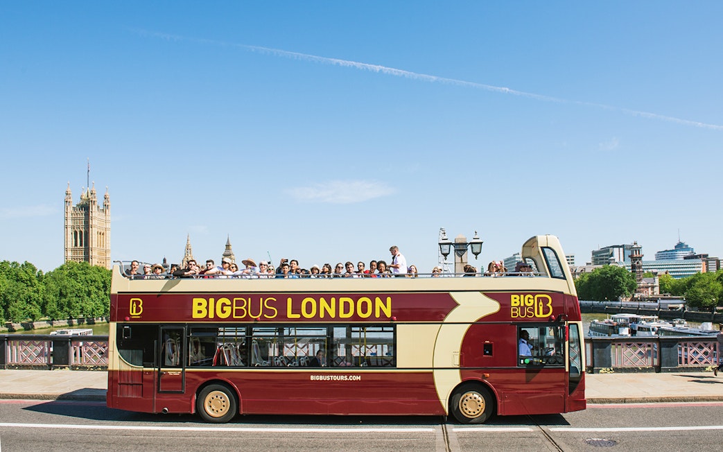 Open-top bus tour in London with tourists, passing by the Houses of Parliament.