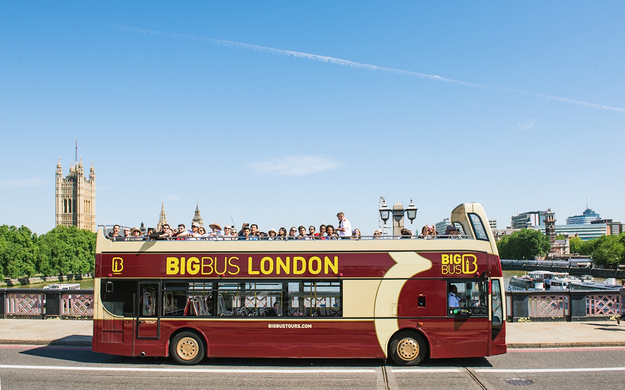 Open-top bus tour in London with tourists, passing by the Houses of Parliament.